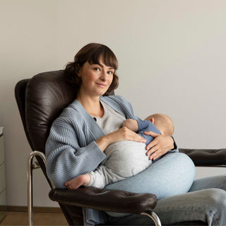Woman breastfeeding a baby in a chair at home with the bbhugme nursing pillow