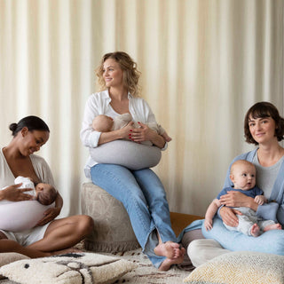 Three women sitting on a couch, each holding a baby and using a bbhugme nursing pillow.