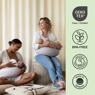 Two women breastfeeding their babies with the bbhugme nursing pillow Oeko-Tex, BPA-free, and Made in Germany certification logos on the right.
