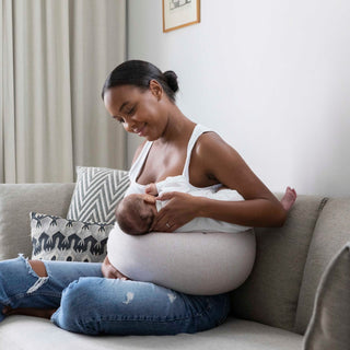 Woman breastfeeding a baby on a couch with the bbhugme nursing pillow in a home setting