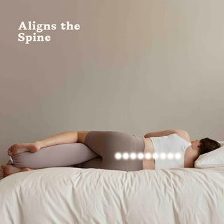 Person lying on a bed with a bbhugme pregnancy pillow under their head, aligning the spine.