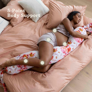 Woman sleeping on a bed with a bbhugme pregnancy pillow, labeled 